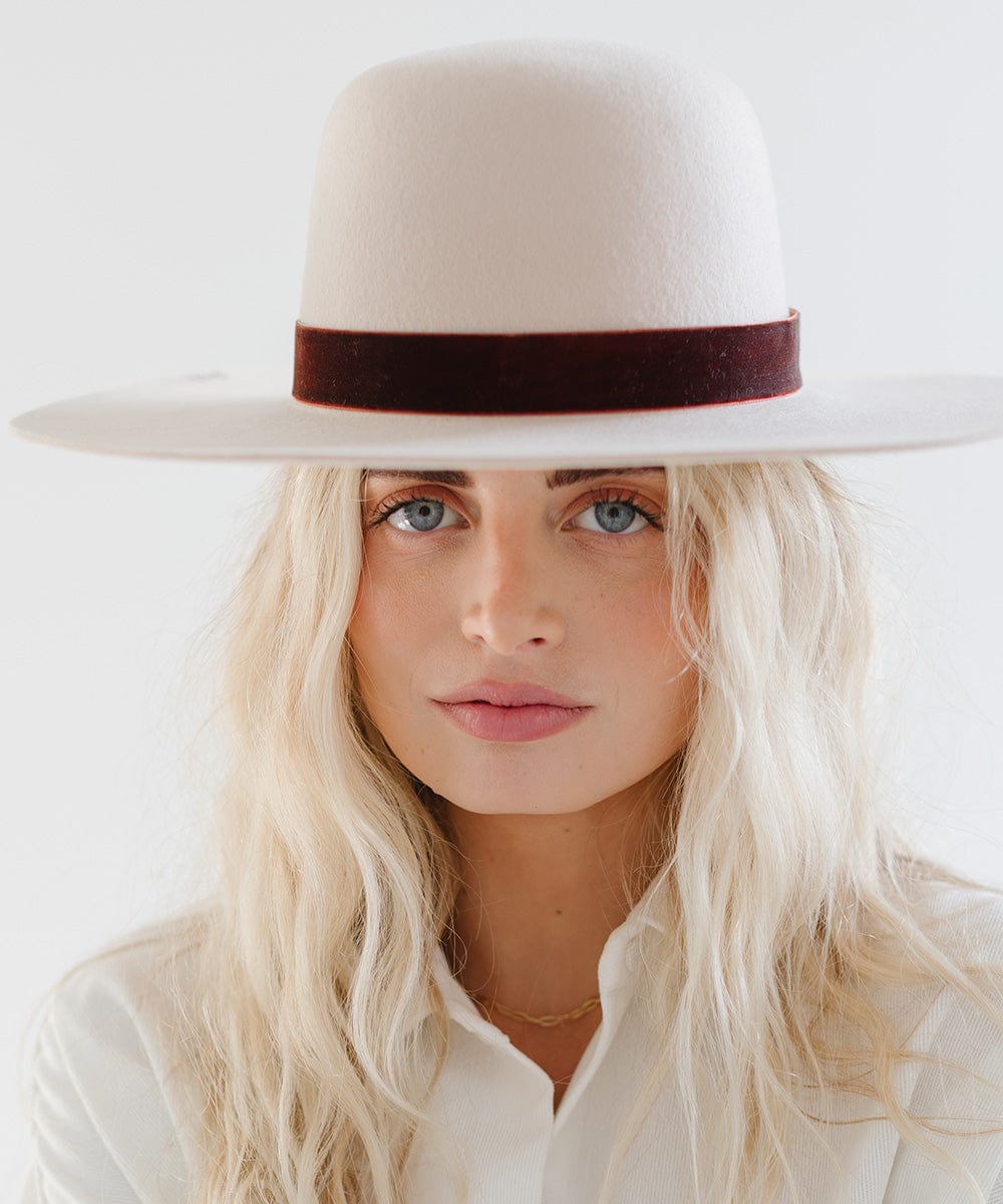 Woman wearing a white hat with a rusty red velvet chain hat band against a plain background #color_rusty red