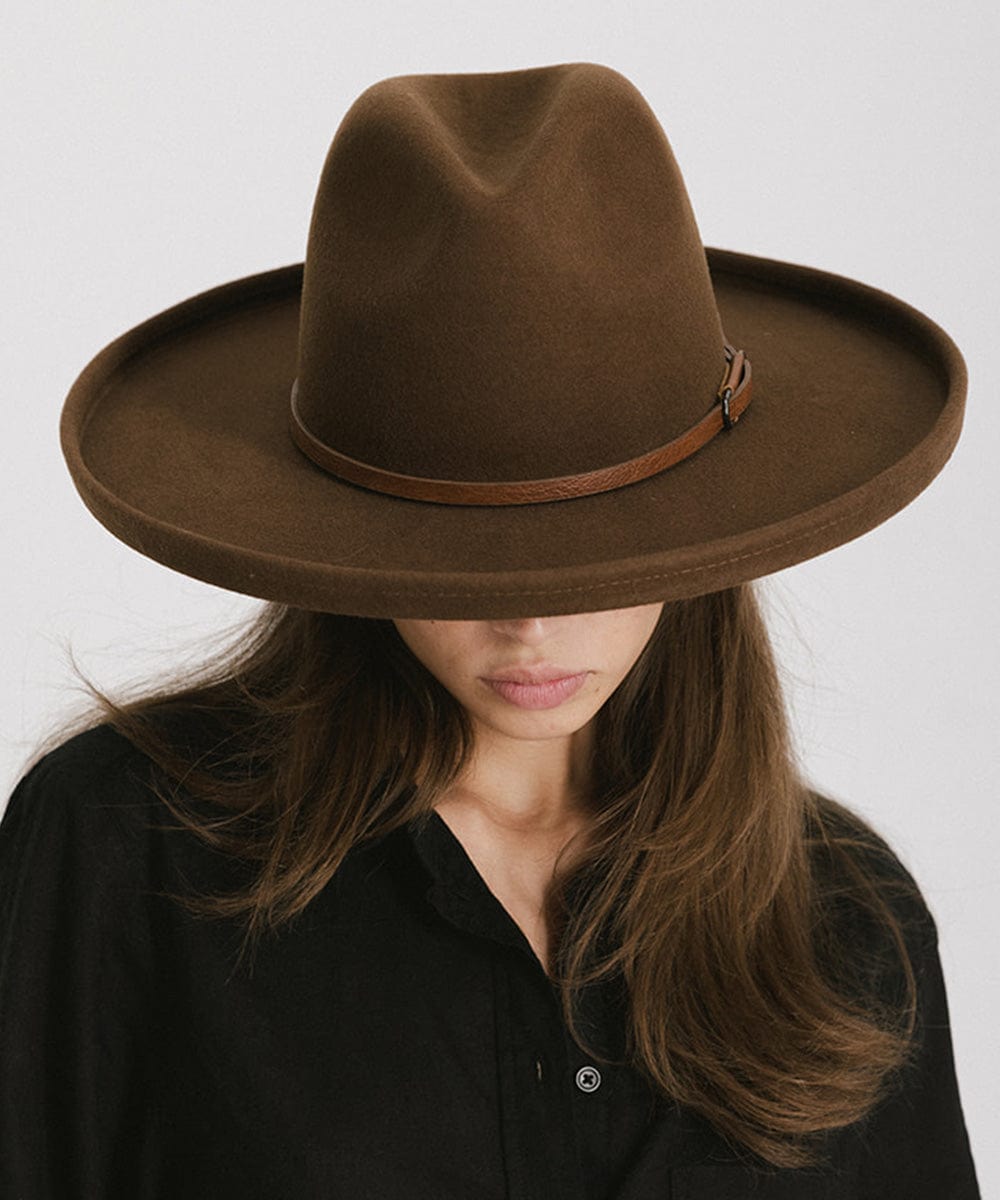 Woman wearing a brown wide-brimmed hat with a brown hat band and a black shirt against a plain background #color_brown