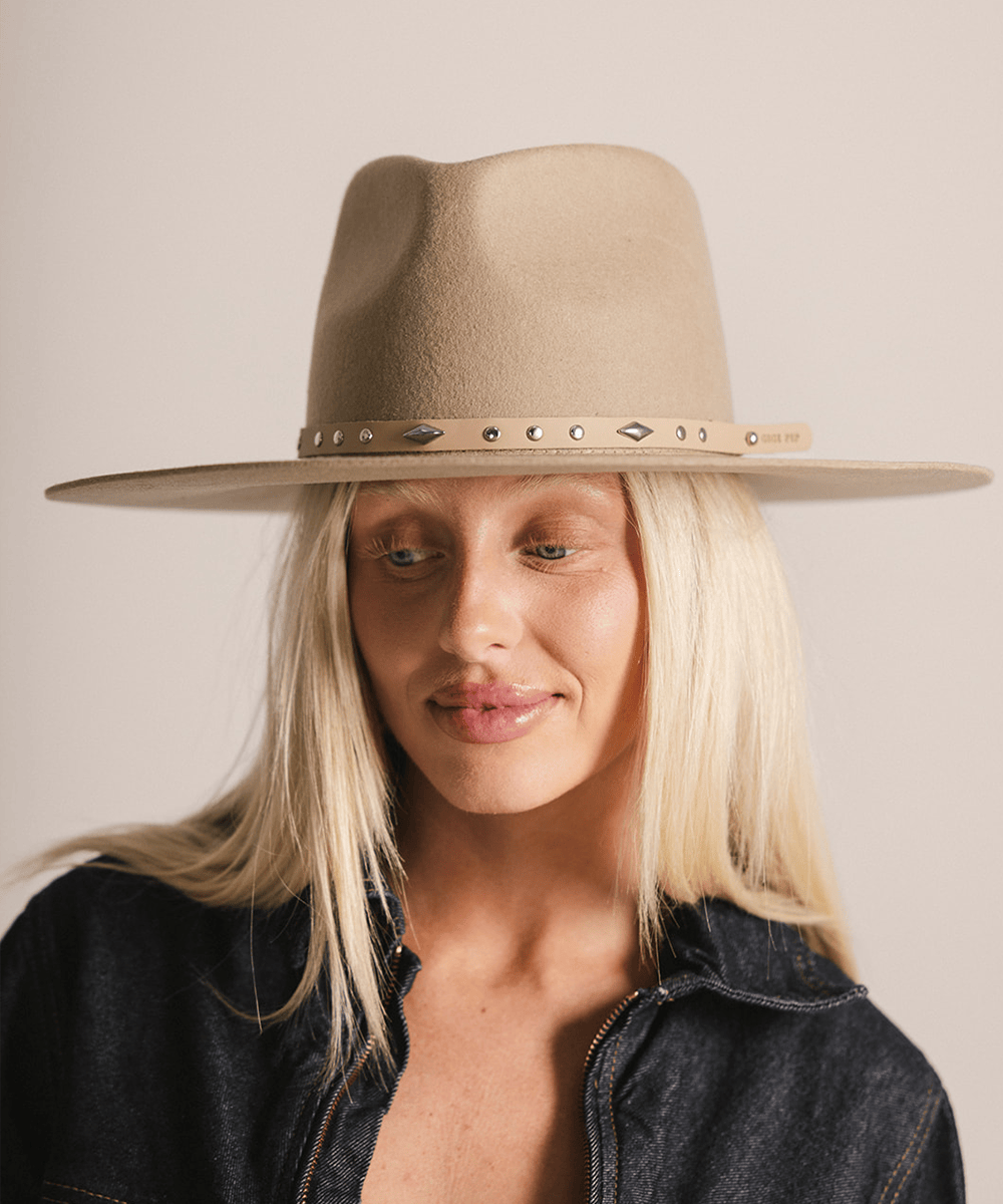 Woman wearing a cream hat with a tan studded leather hat band against a plain background #color_tan