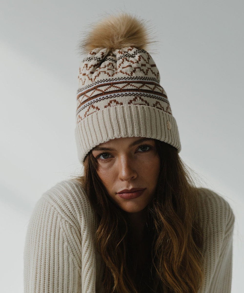 Woman wearing a printed knit beanie and a white sweater against a plain background