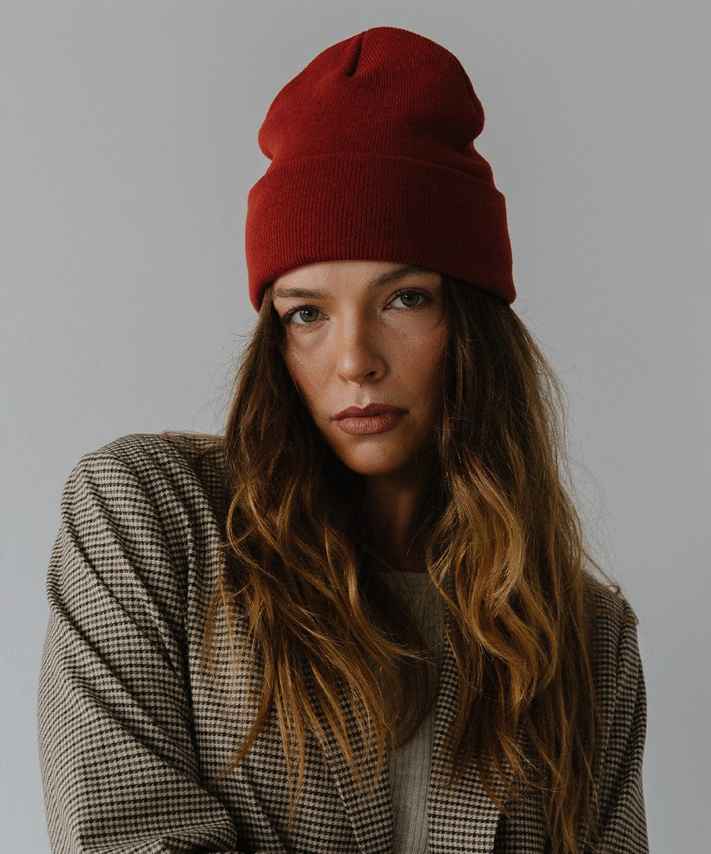 Woman wearing a brick red colored beanie and a coat against a plain background #color_brick red