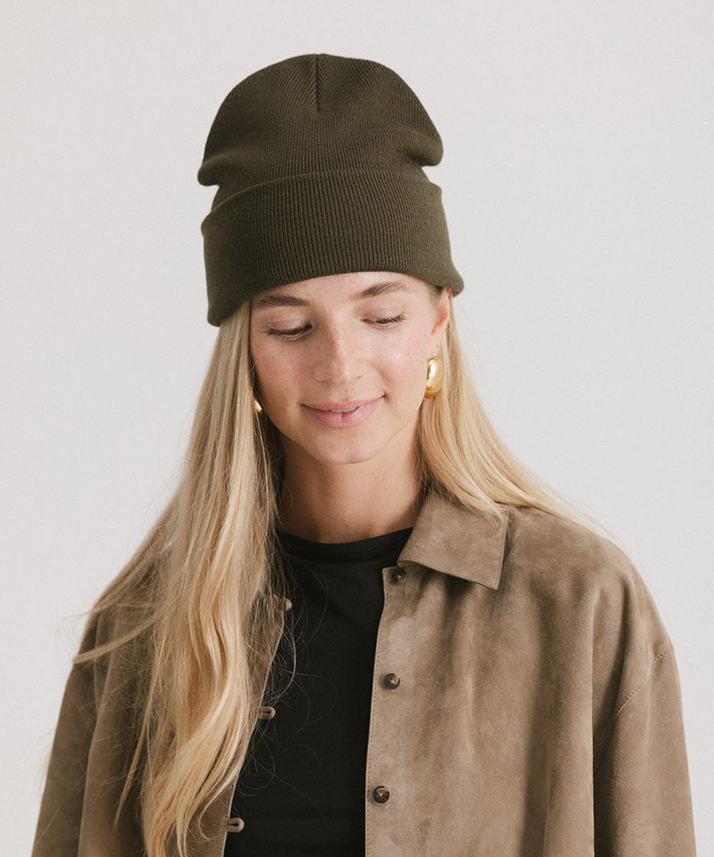 Woman wearing a dark green beanie and a black t-shirt with a beige shirt against a plain background #color_dark green