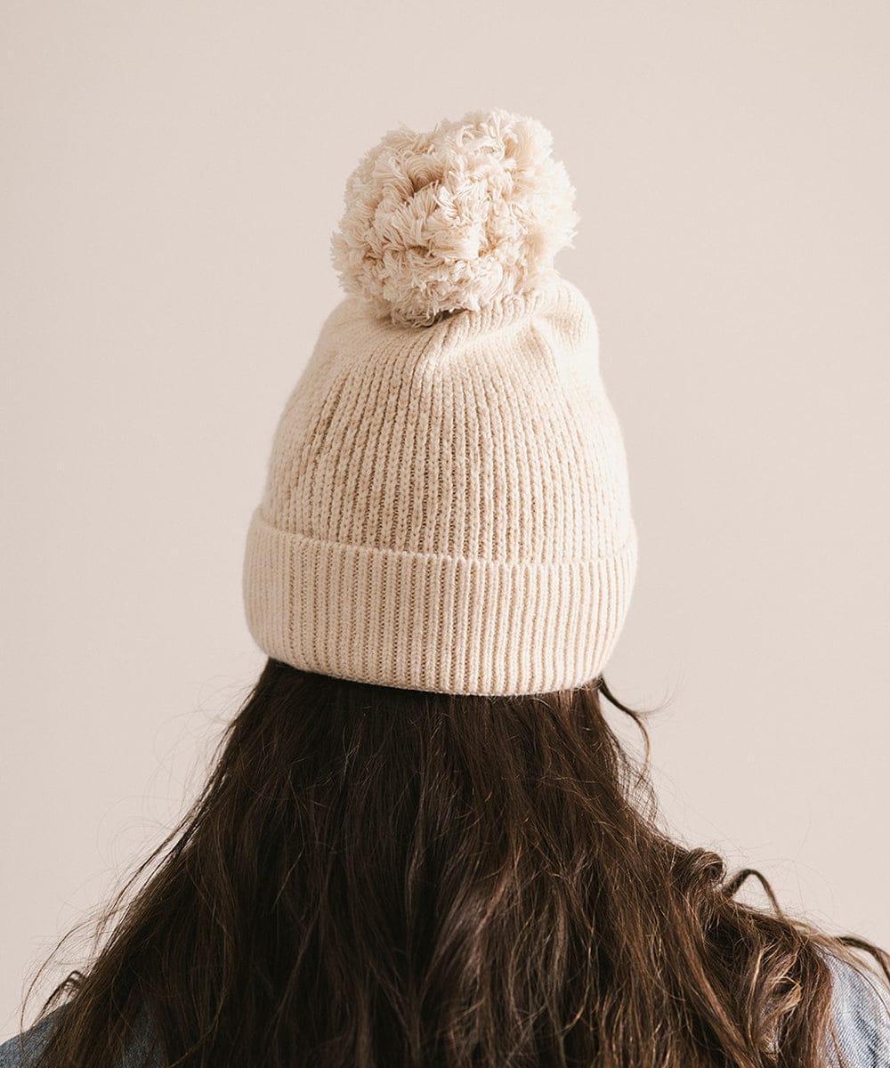 Person wearing a cream knit beanie with a pom-pom on a plain background #color_cream