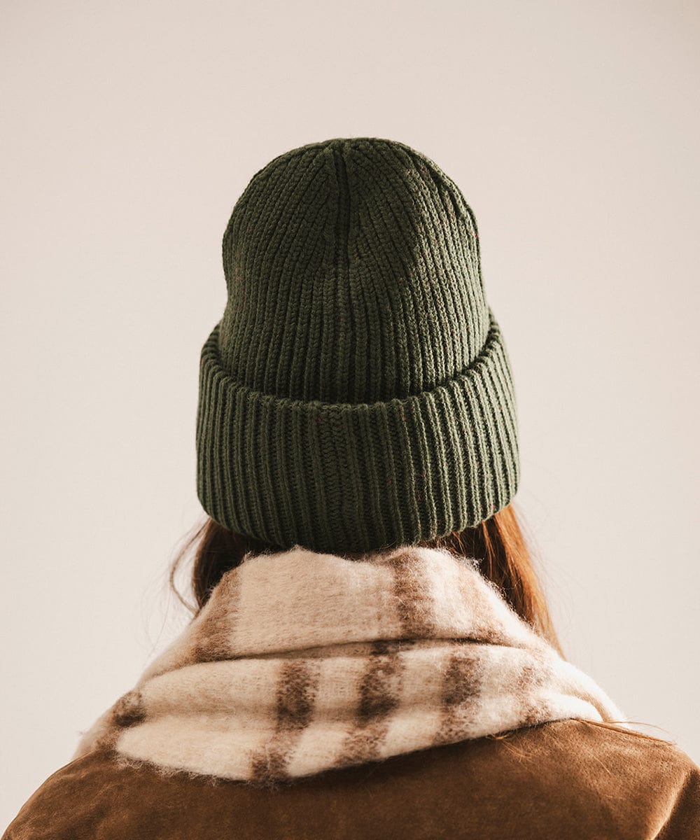 A woman wearing a dark green chunky ribbed beanie, facing behind against a plain background #color_dark green
