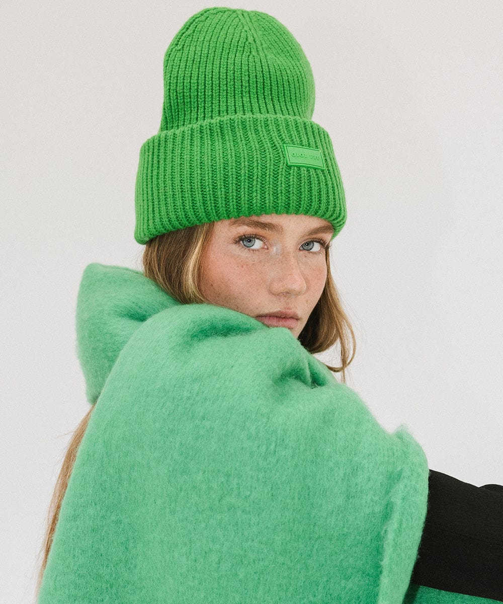 A woman wearing an evergreen colored ribbed beanie and a green top against a plain background #color_evergreen