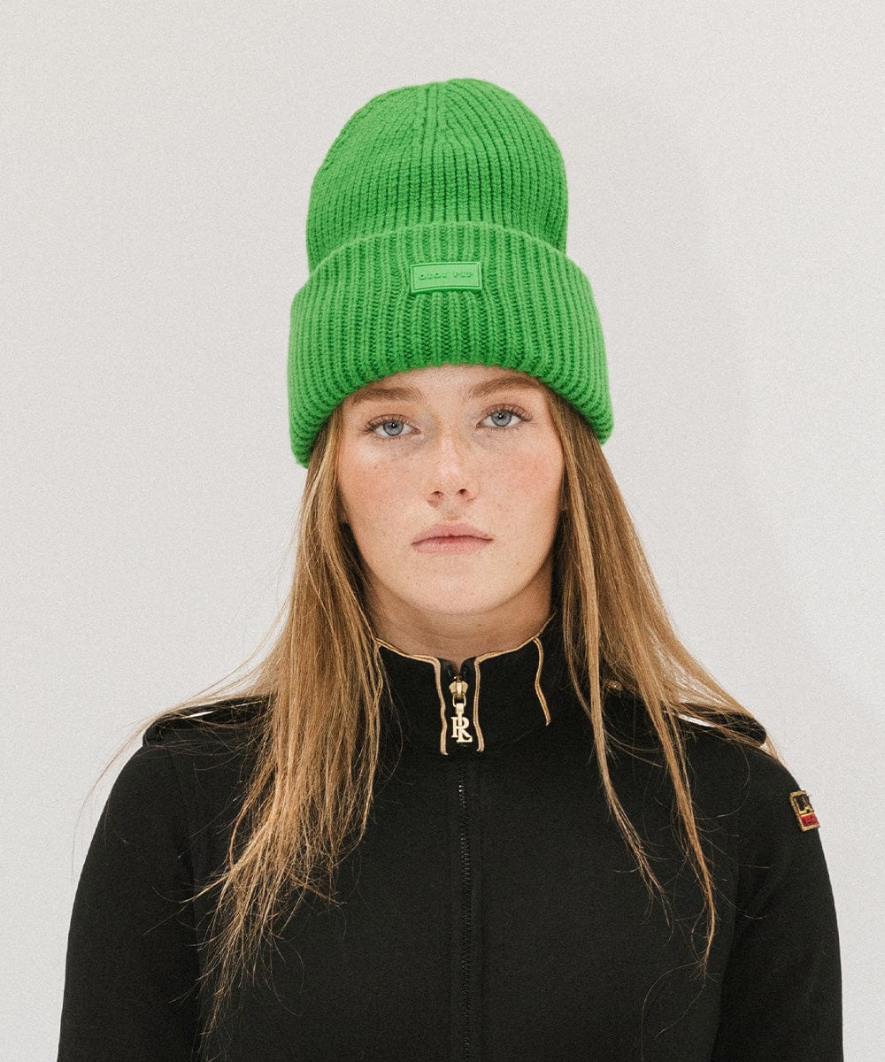A woman wearing an evergreen colored ribbed beanie and a black jacket against a plain background #color_evergreen