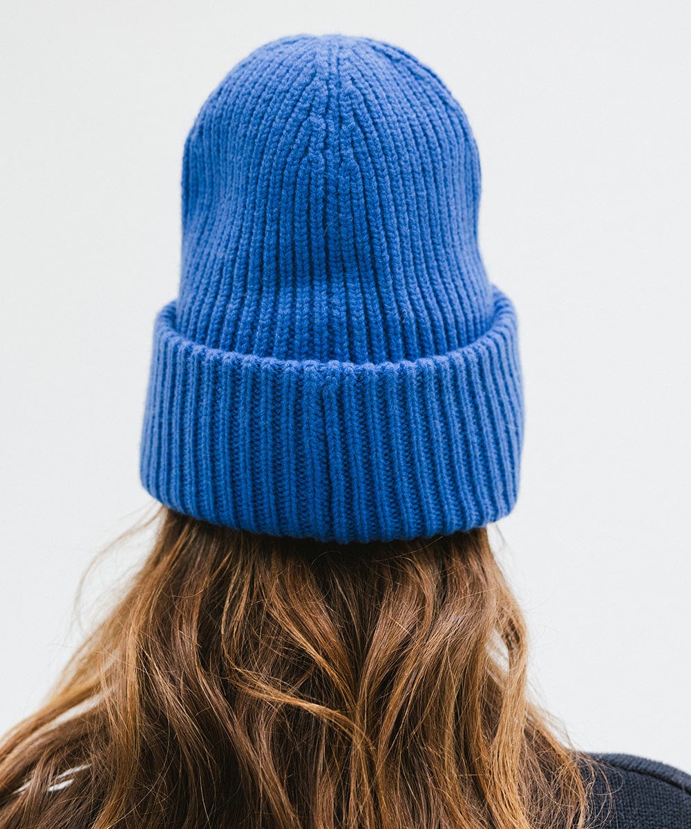 A person wearing an alpine blue colored ribbed beanie facing behind against a plain background #color_alpine blue