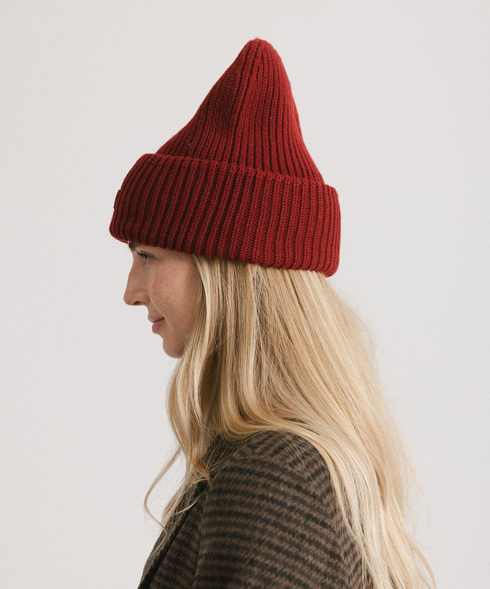 A woman wearing a burgundy ribbed beanie, facing sideways against a plain background #color_burgundy