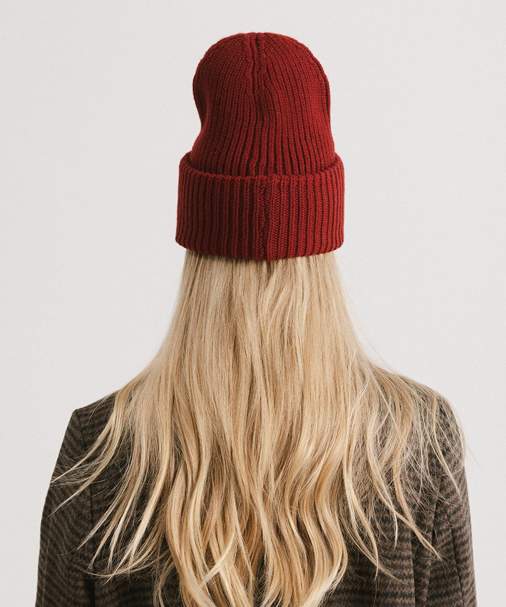 Person with long blonde hair wearing a burgundy ribbed beanie, facing behind against a plain background #color_burgundy