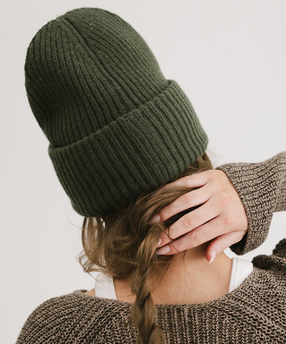 A person wearing a dark green chunky ribbed beanie facing behind against a plain background #color_dark green