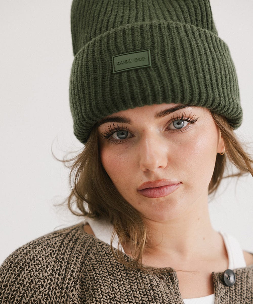A woman wearing a dark green chunky ribbed beanie against a plain background #color_dark green