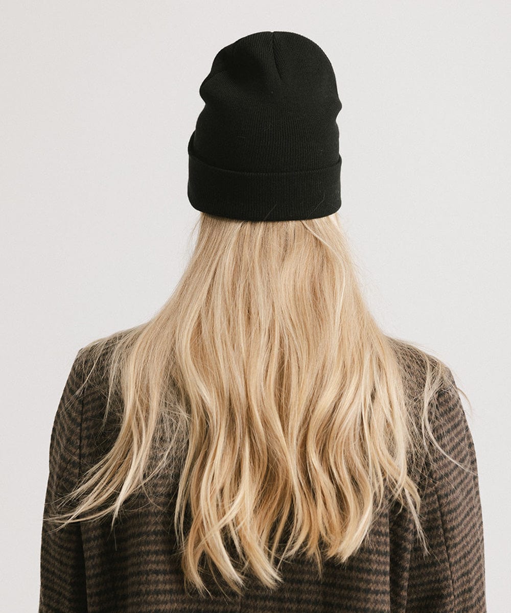 Woman with blonde hair wearing a black beanie and a coat, facing behind against a plain background #color_black