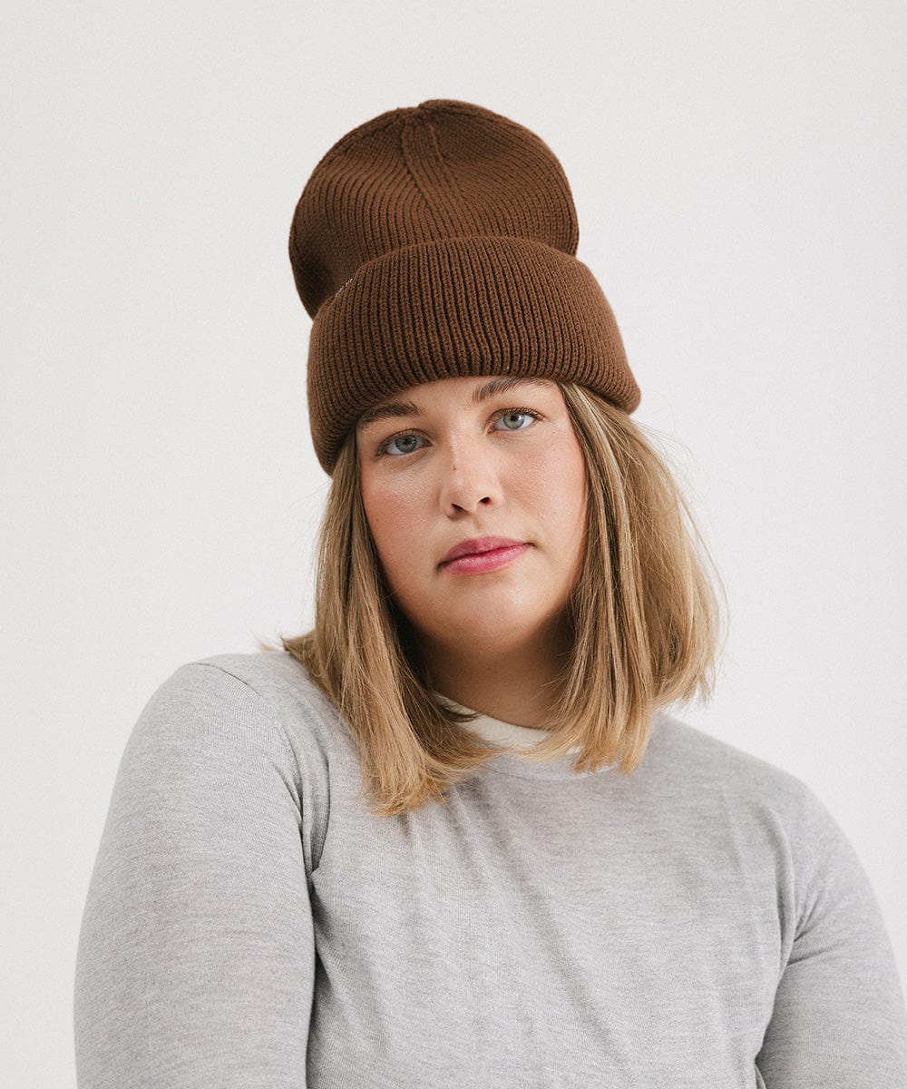 Woman wearing a chocolate colored oversized knit beanie and a grey t-shirt against a plain background #color_chocolate