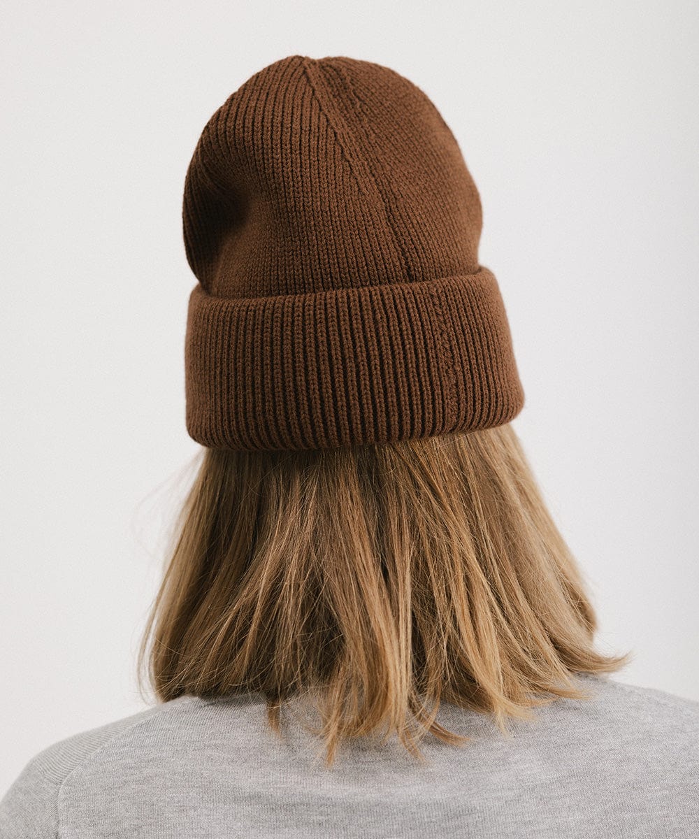 Person wearing a chocolate colored oversized knit beanie against a plain background #color_chocolate