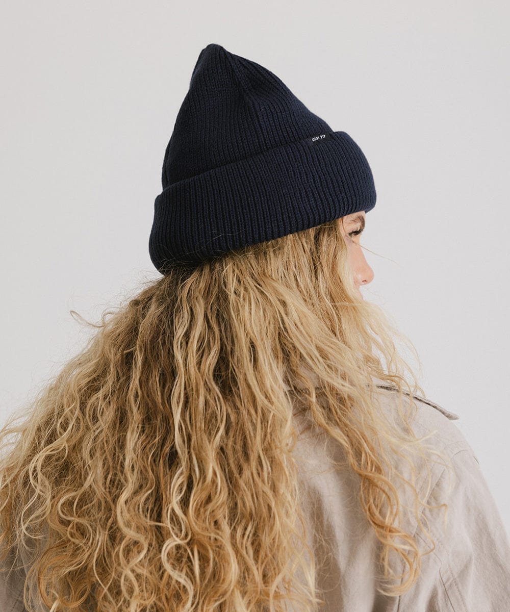 Woman with long blonde hair wearing a navy oversized knit beanie against a plain background #color_navy