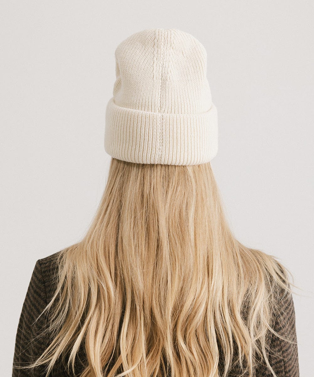 Person with long blonde hair wearing an off white oversized knit beanie against a plain background #color_off white