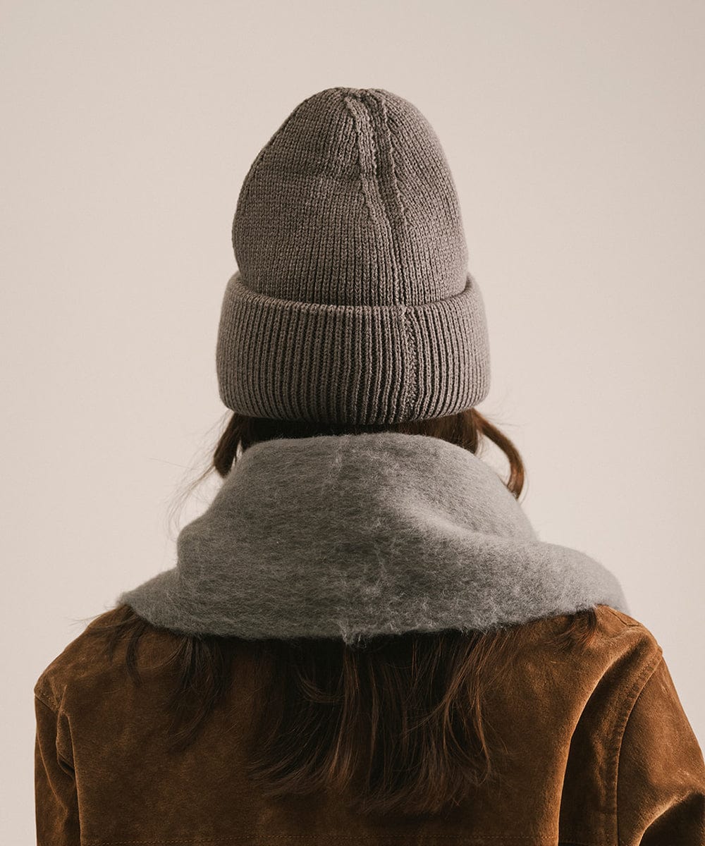 Person wearing a gray knit beanie and scarf with a brown coat on a plain background #color_grey