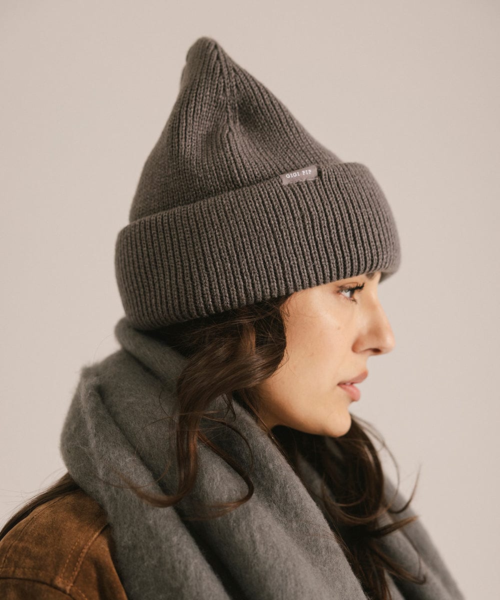 Woman wearing a gray knit beanie and scarf against a neutral background #color_grey