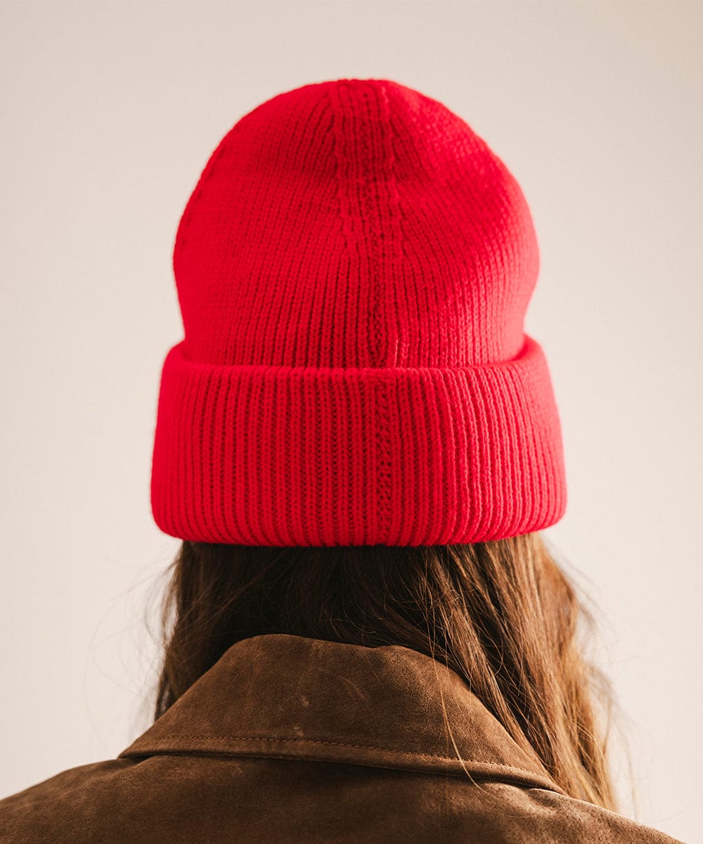 Person wearing a red knit beanie and brown jacket on a plain background #color_red