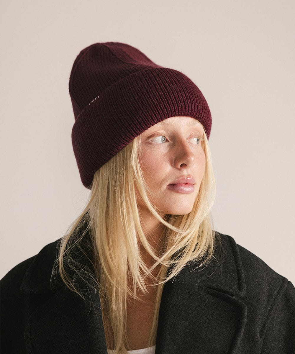 Person wearing a maroon beanie and dark coat against a plain background #color_merlot