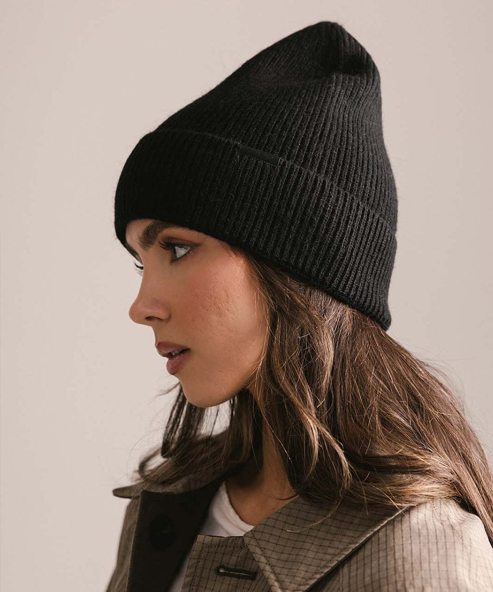 Woman wearing a black knit beanie against a neutral background #color_black