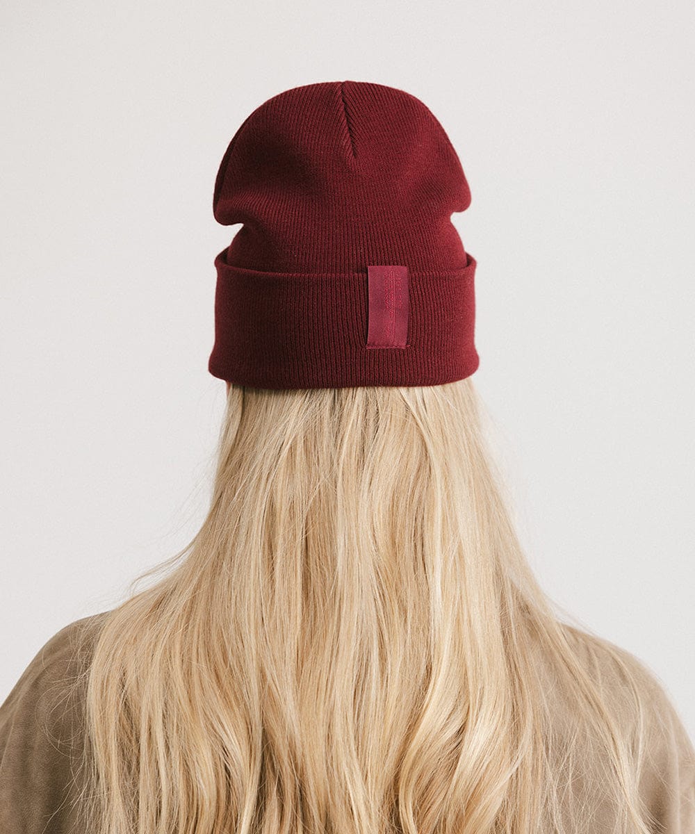 Woman with blonde hair wearing a burgundy beanie facing behind against a plain background #color_burgundy