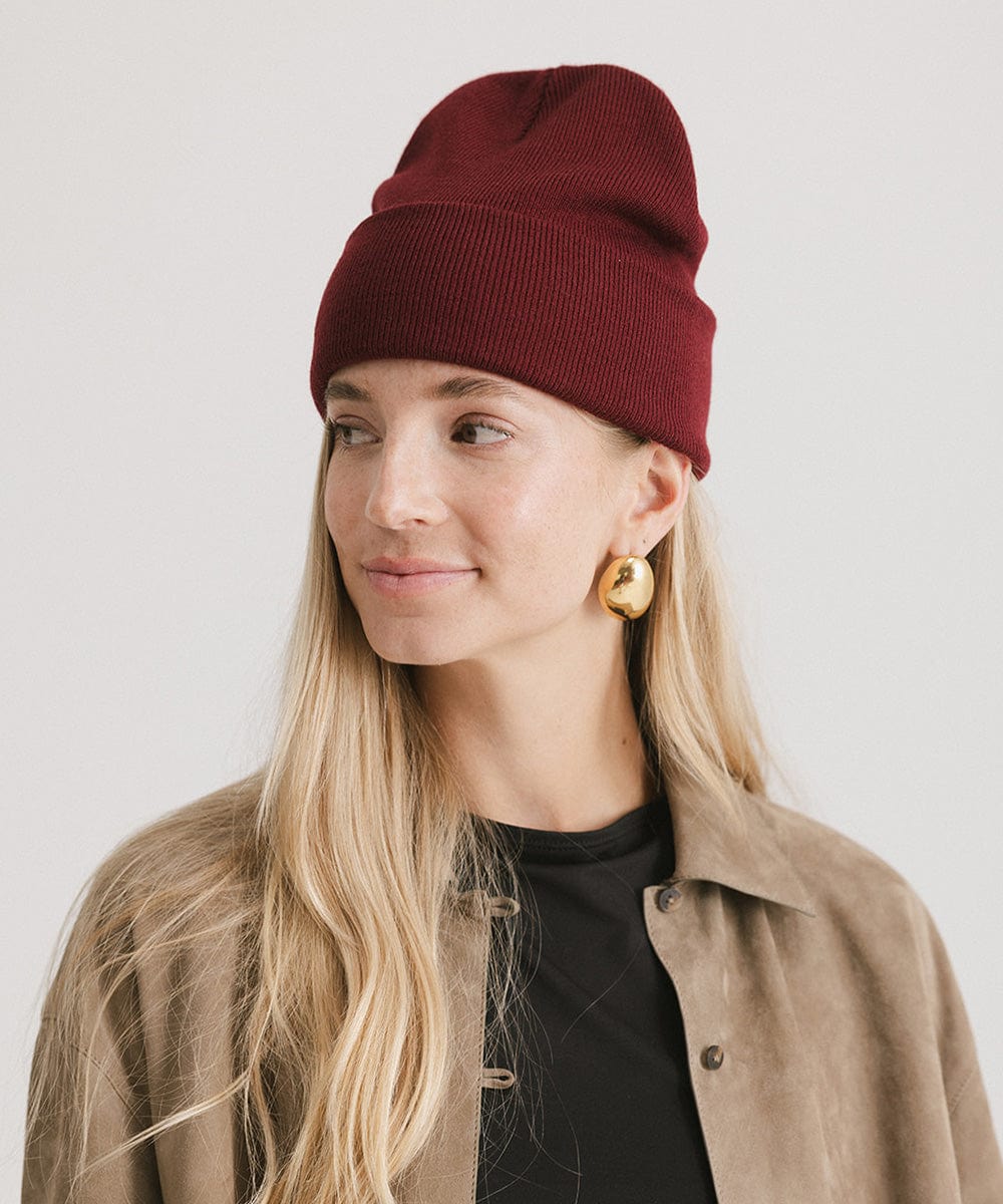 Woman wearing a burgundy beanie and a black t-shirt with a beige shirt against a plain background #color_burgundy