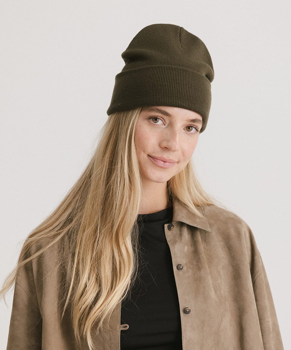 Woman wearing a dark green beanie and black t-shirt with a beige shirt against a plain background #color_dark green