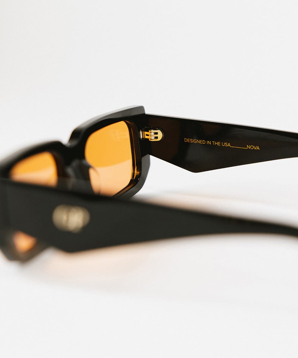 Close up image of sunglasses with black frame and orange lenses on a white background #color_black