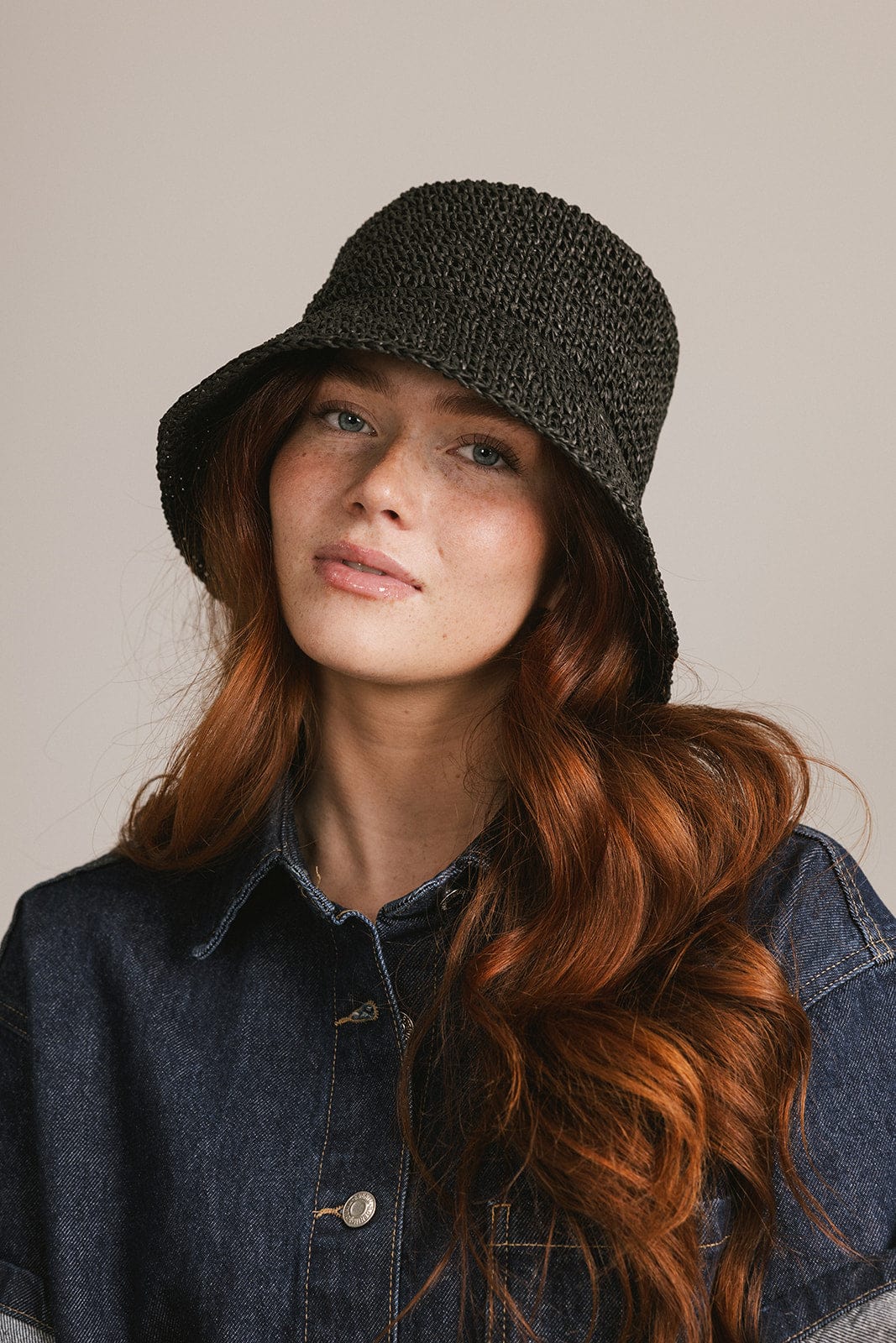 Woman wearing a black crochet packable bucket hat and a denim shirt against a plain background #color_black