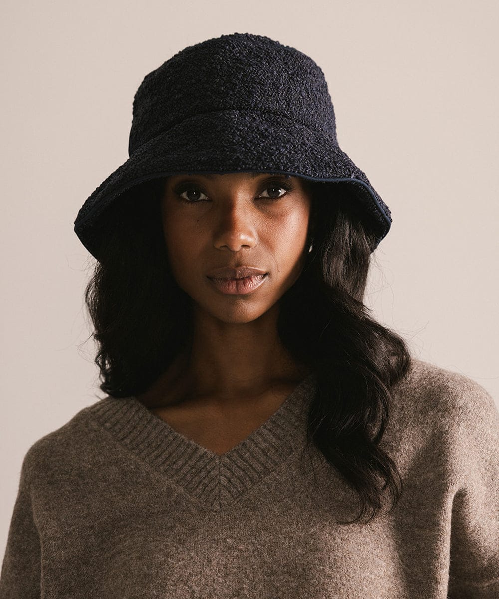 Woman wearing a dark blue textured hat and brown sweater against a neutral background #color_navy