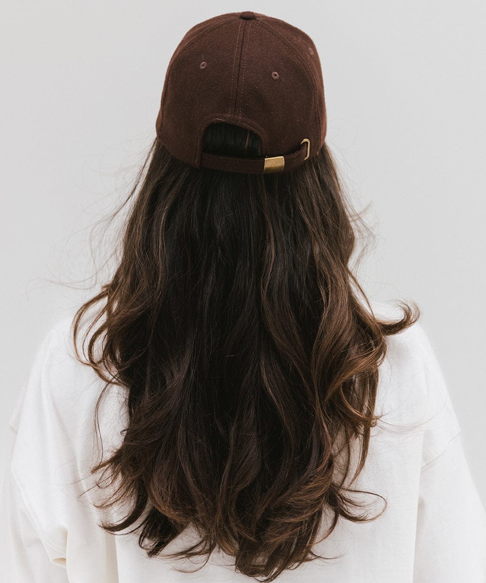 Woman with long hair wearing a chocolate brown baseball cap and a white top against a plain background #color_chocolate brown
