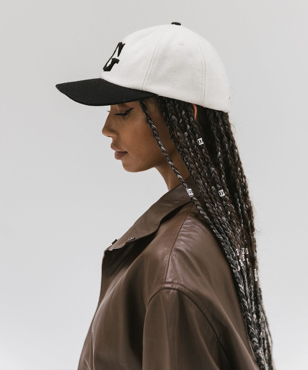 Woman wearing a cream and black baseball cap and a brown jacket, facing sideways against a plain background #color_cream-black