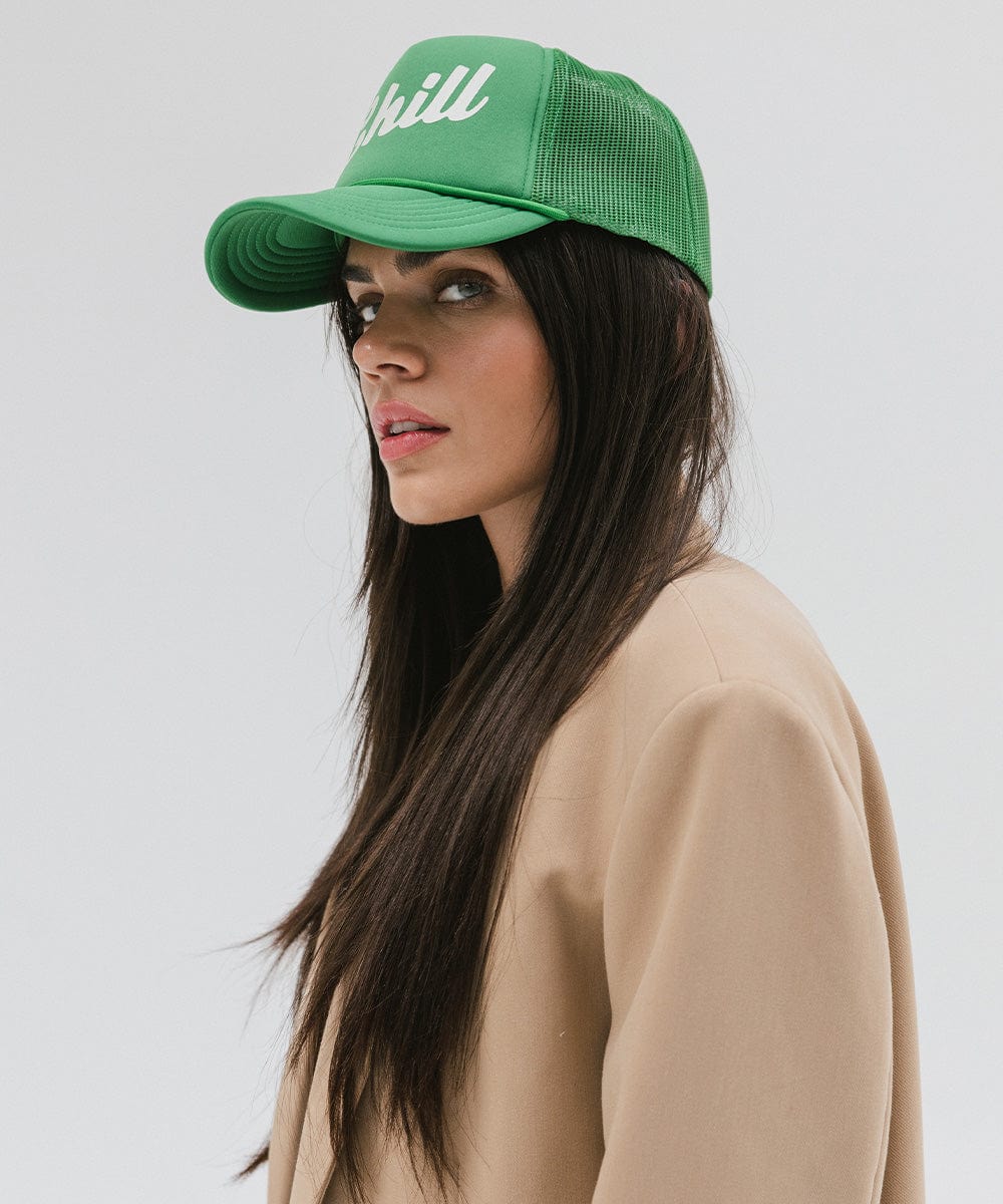 Woman wearing a vintage green colored trucker hat with the text 'Chill' and a beige blazer against a plain background #color_vintage green