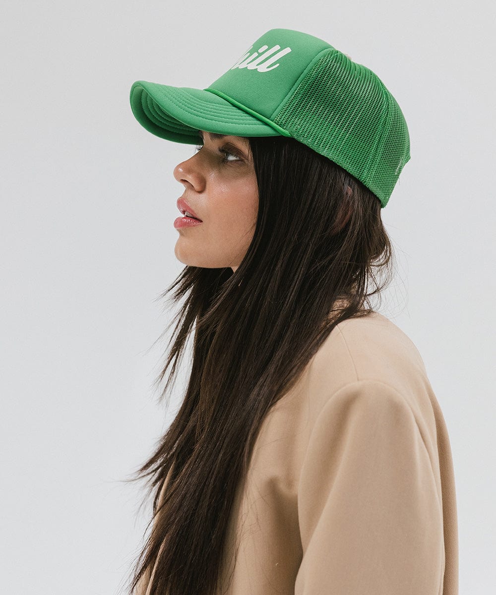 Woman wearing a vintage green colored trucker hat and a beige blazer, facing sideways against a plain background #color_vintage green