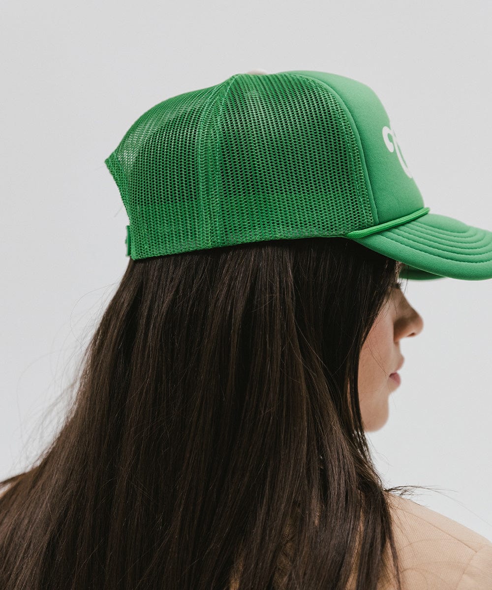 Woman wearing a vintage green colored trucker hat looking sideways against a plain background #color_vintage green