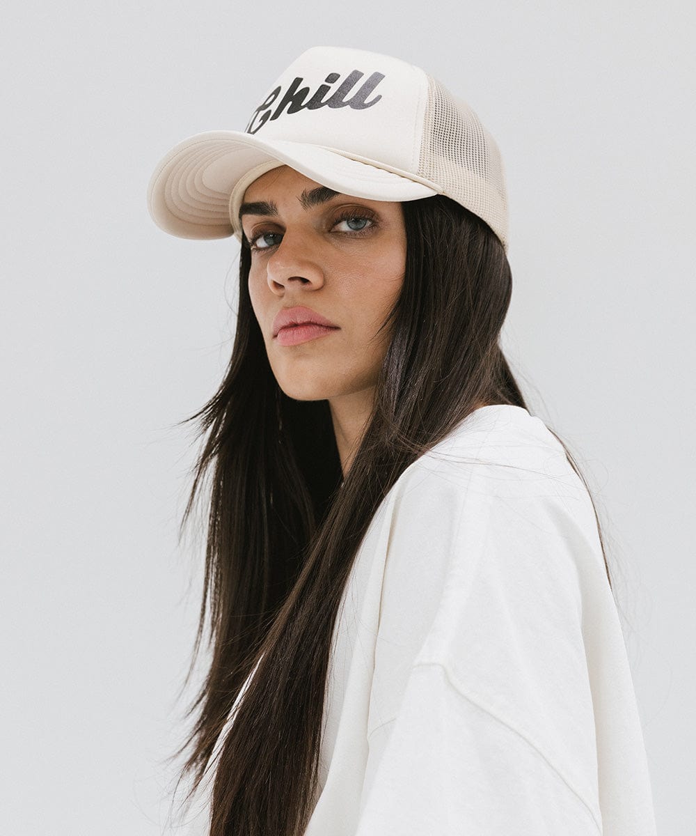 Woman wearing a cream trucker hat with the text 'Chill' and a white t-shirt, posing against a plain background #color_cream