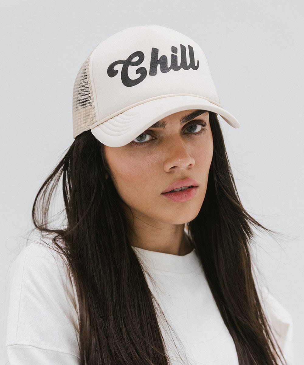 Woman wearing a cream trucker hat with the text 'Chill' and a white t-shirt against a plain background #color_cream
