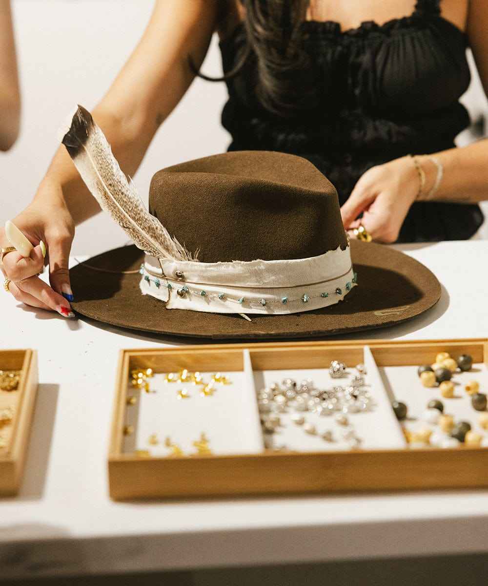 Brown hat with decorative band held by a person, with jewelry box in the foreground