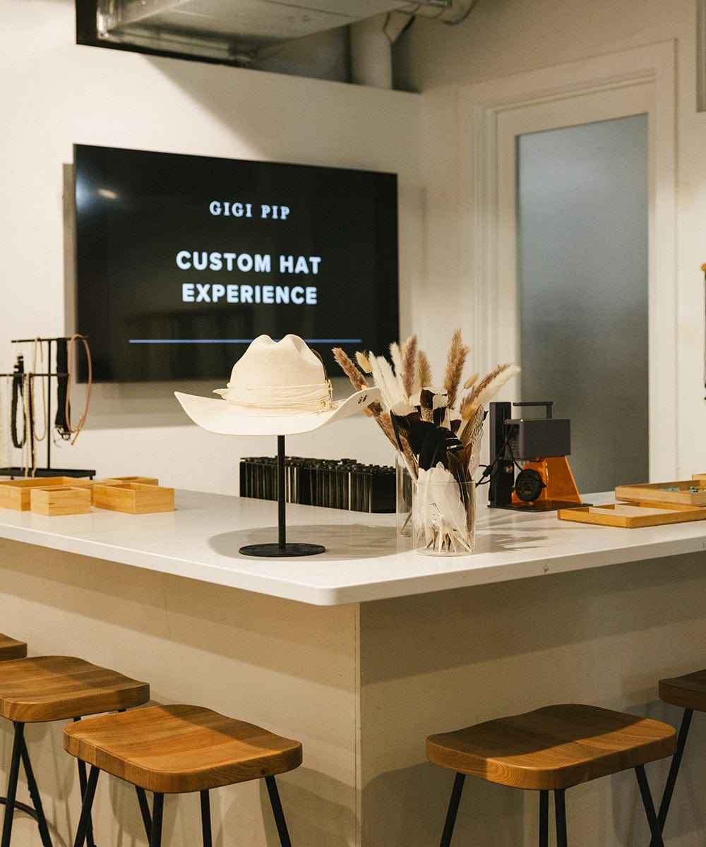 Interior of a store with a counter displaying a white hat, TV screen, and wooden stools.
