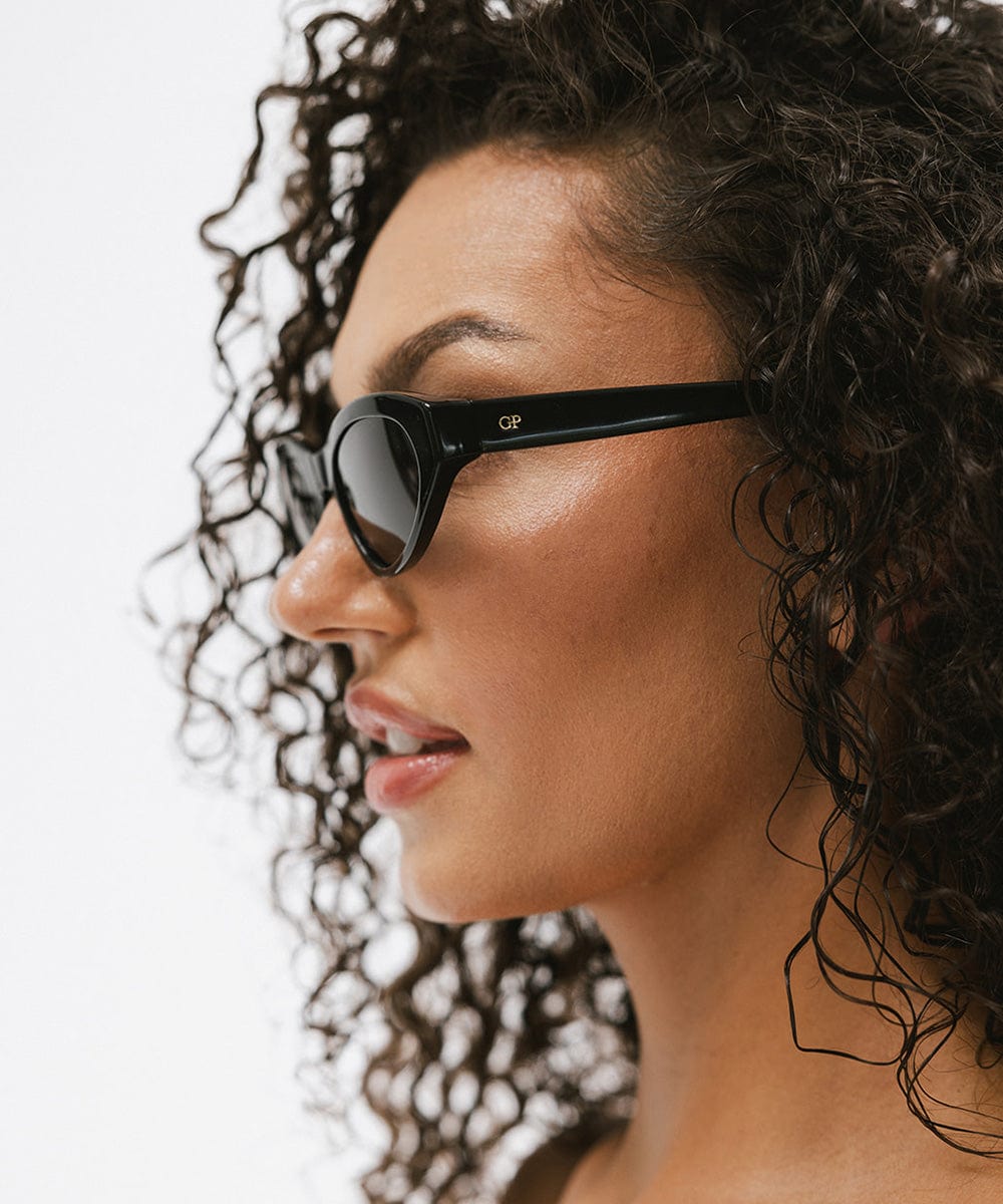 Woman wearing black colored cat eye sunglasses facing sideways against a white background #color_black