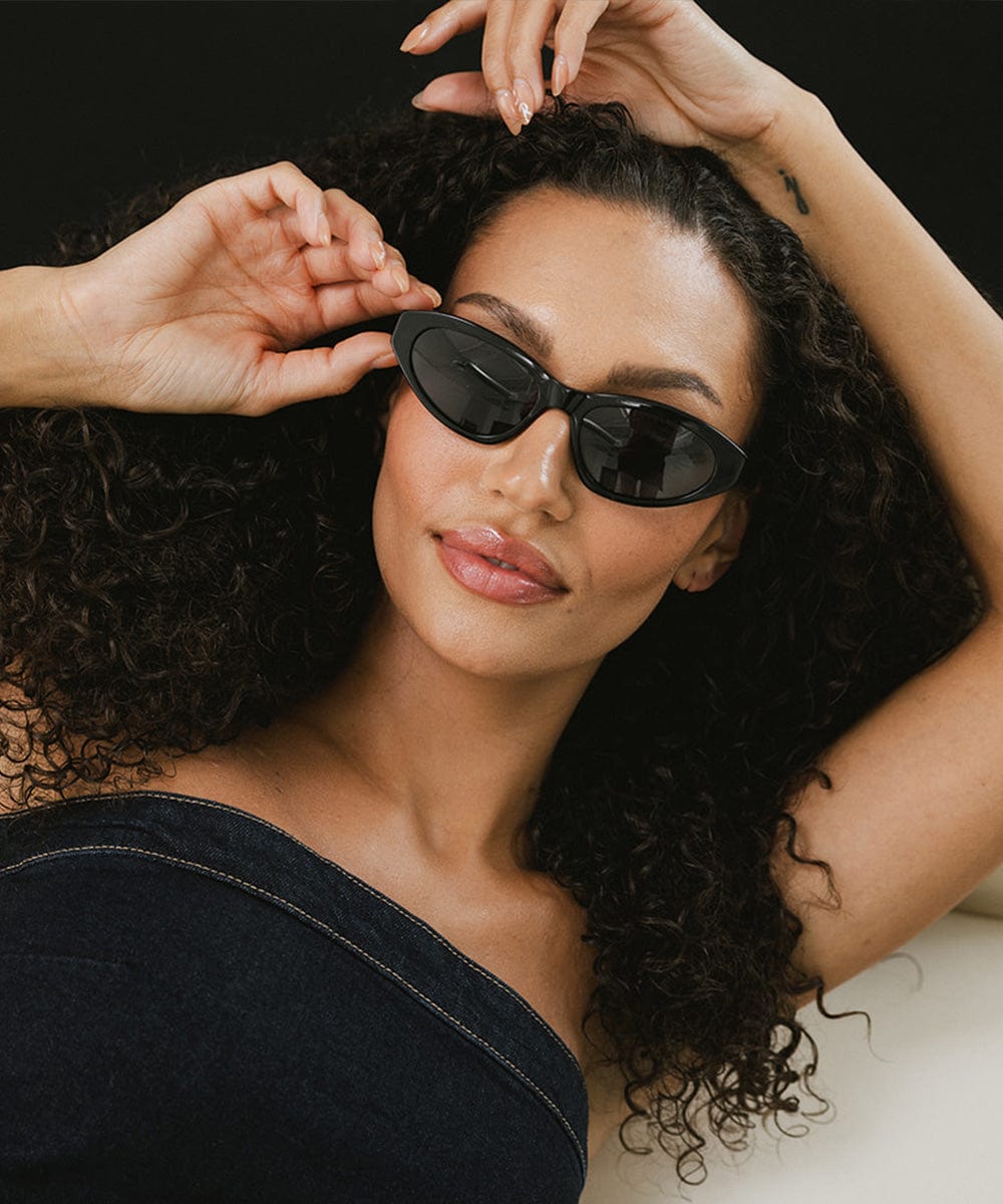 Woman wearing black colored cat eye sunglasses and a denim top against a black background #color_black