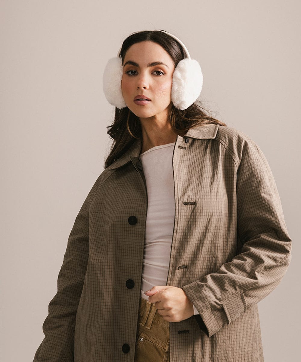 Woman wearing a beige coat and white ear muffs against a plain background #color_winter white