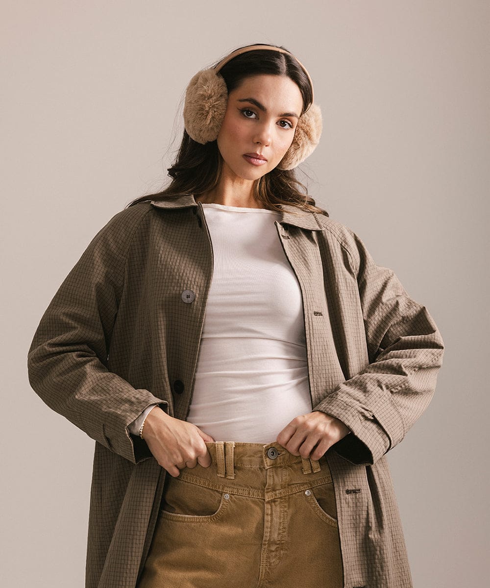 Woman wearing a brown coat, white shirt, and tan pants with brown ear muffs on a plain background #color_tan