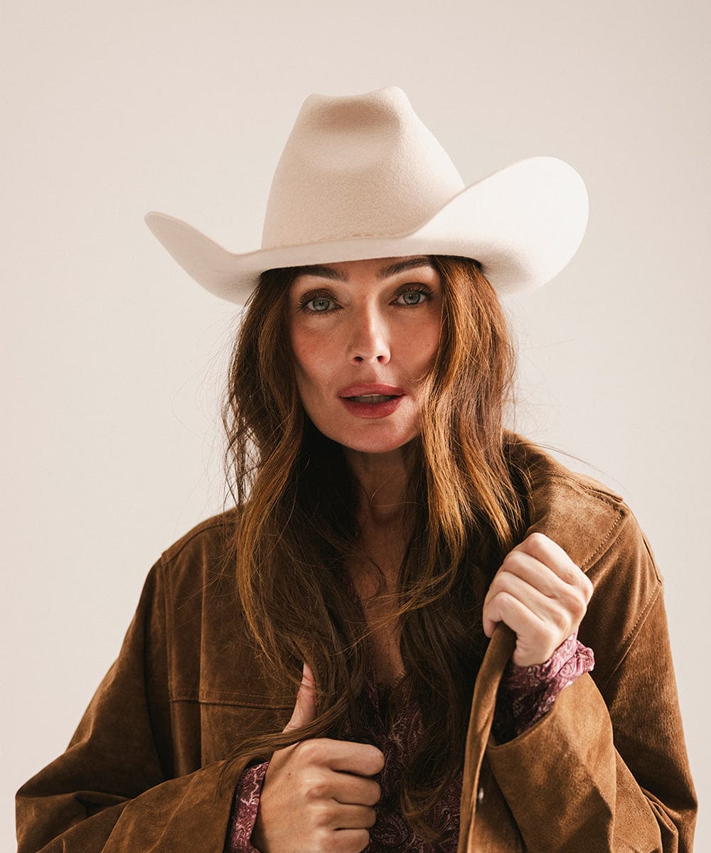Woman wearing a white cowboy hat and brown jacket against a plain background #color_cream