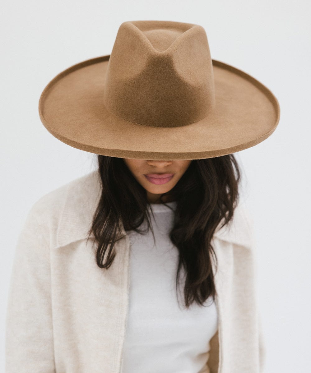 Woman wearing a brown pencil brim fedora hat and a white top with a cream jacket, looking down against a white background #color_brown