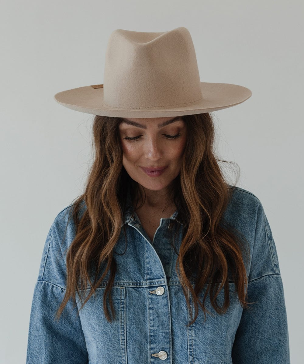 Woman wearing a cream fedora hat and a denim shirt, looking down against a plain background #color_cream