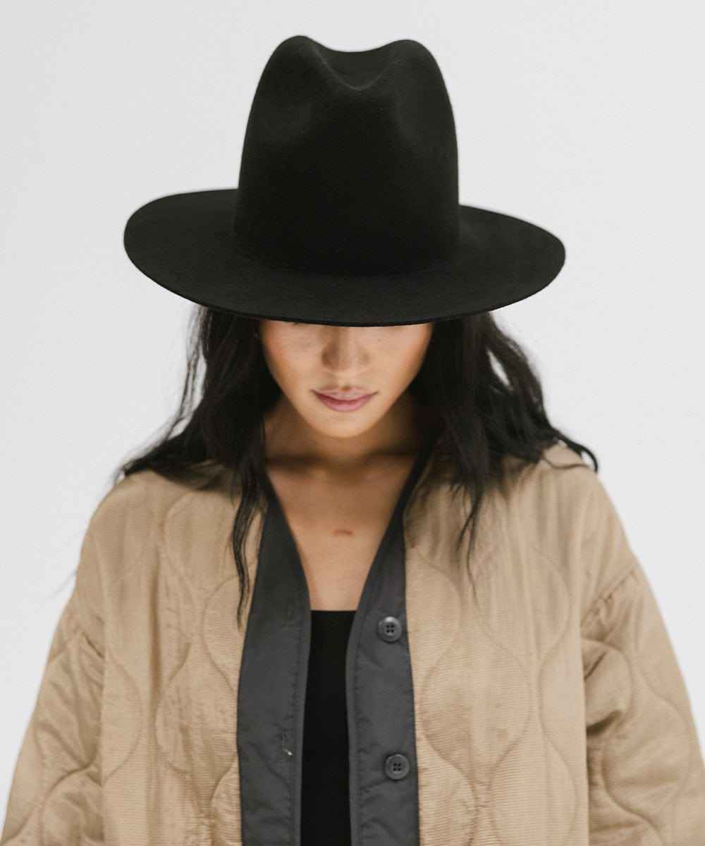 Woman wearing a black tall fedora hat and a beige jacket against a plain background #color_black