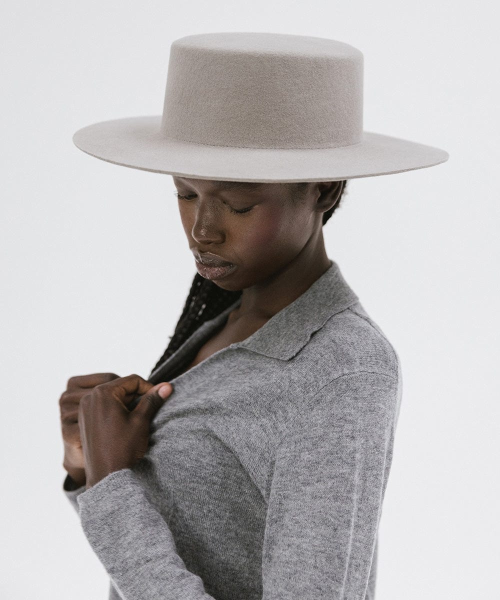 Woman wearing a light grey boater-style hat and a grey shirt against a plain background #color_light grey