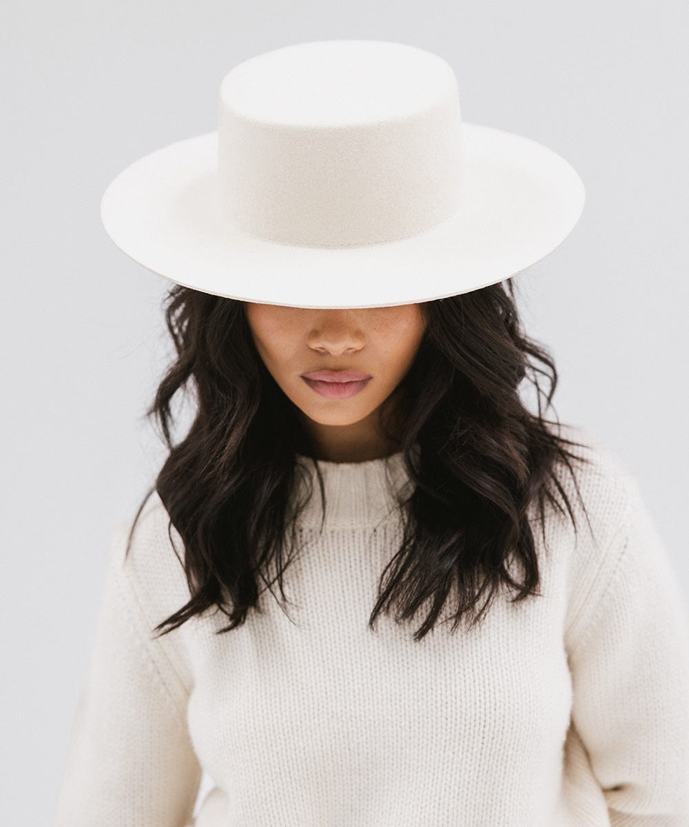 Woman wearing an off white boater-style hat and a white sweatshirt against a plain background #color_off white